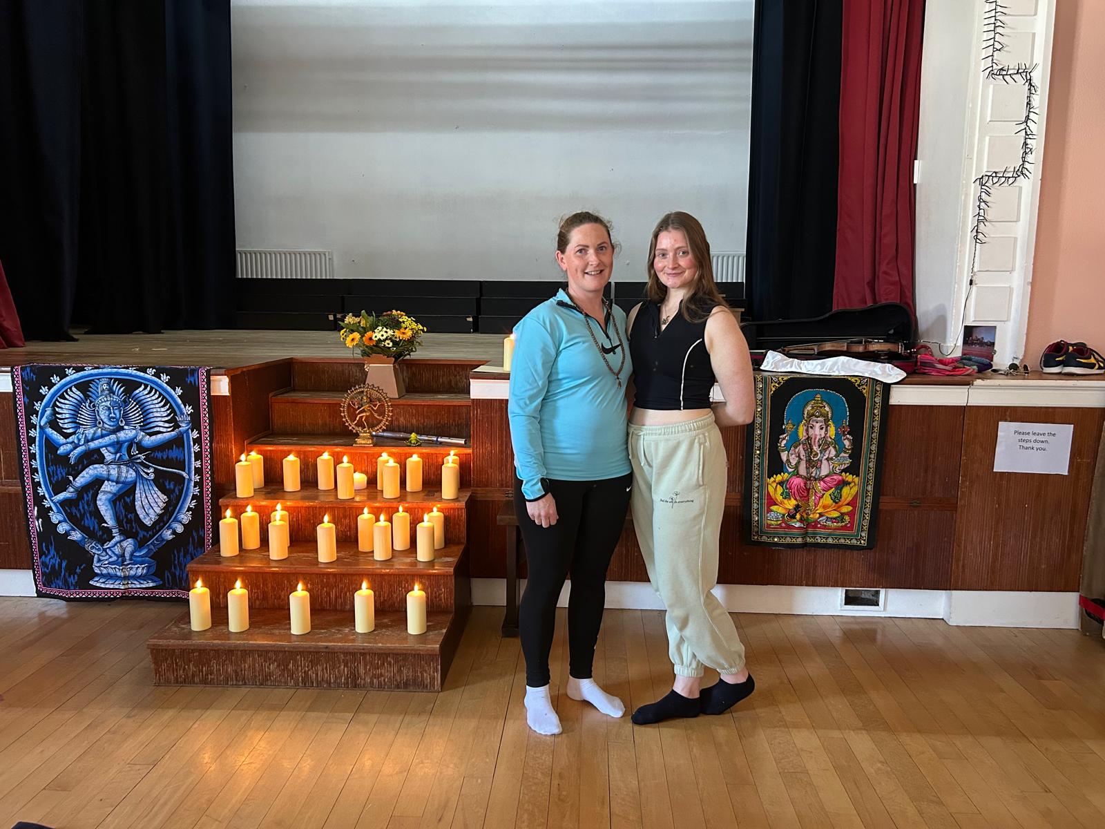 Two graduates together beside the candles and Nataraja hanging