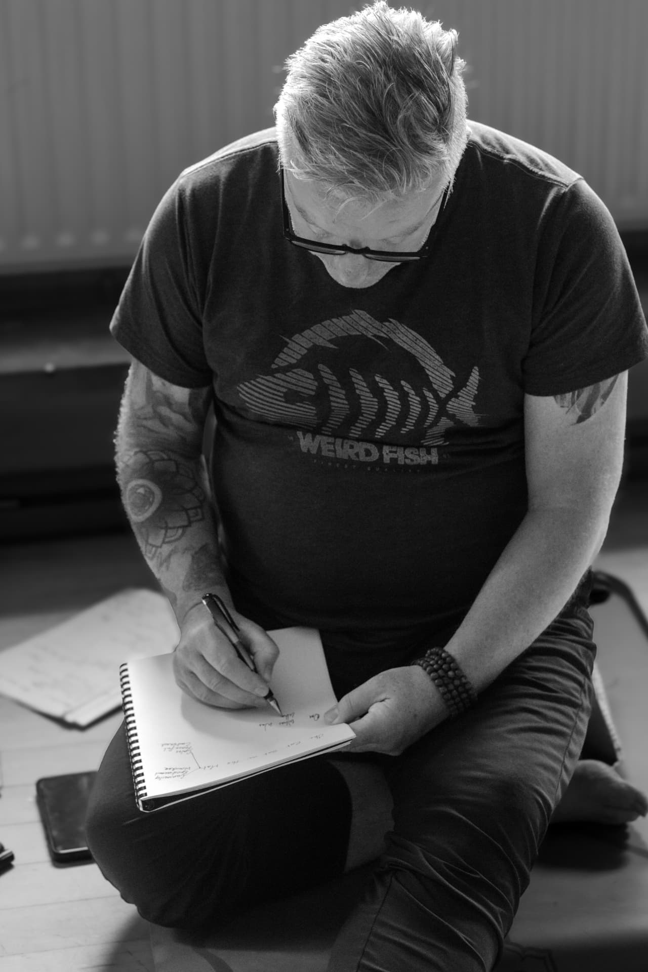 Black-and-white photograph of Michael Connolly writing notes in a notebook while seated on the studio floor