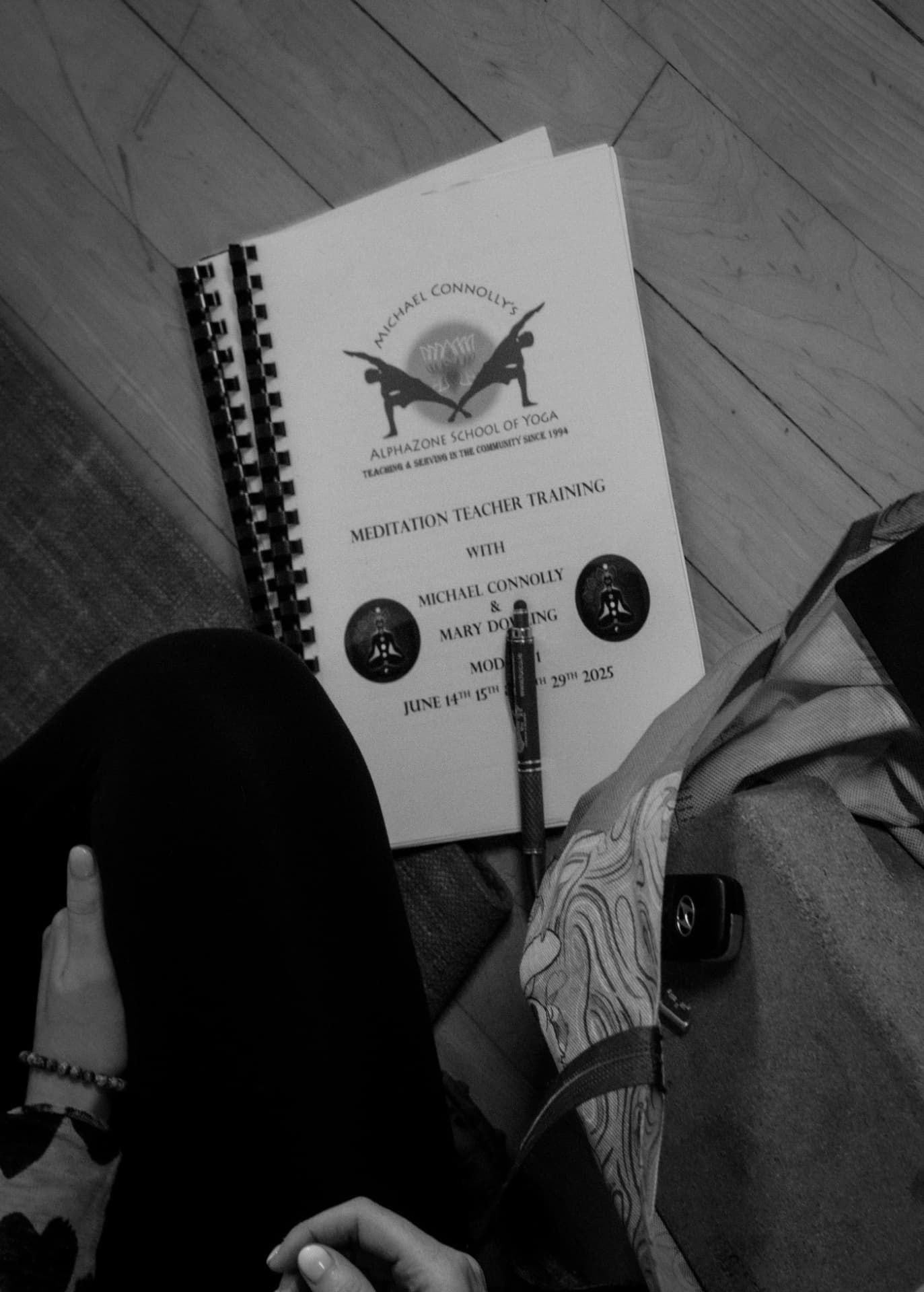 The AlphaZone Meditation Teacher Training workbook resting on a wooden floor beside a pen