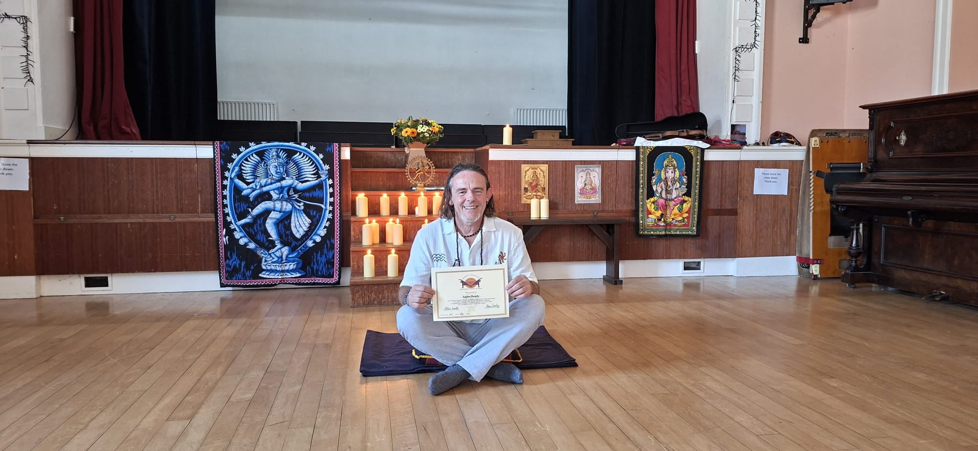 A graduate seated cross-legged holding his AlphaZone certificate